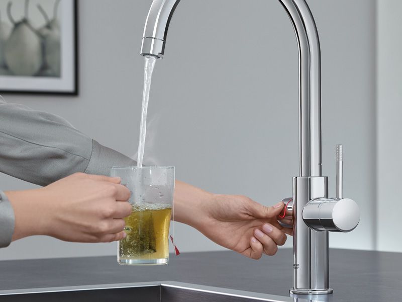 grohe Moderne Armatur füllt heißes Wasser in ein Glas mit Teebeutel.