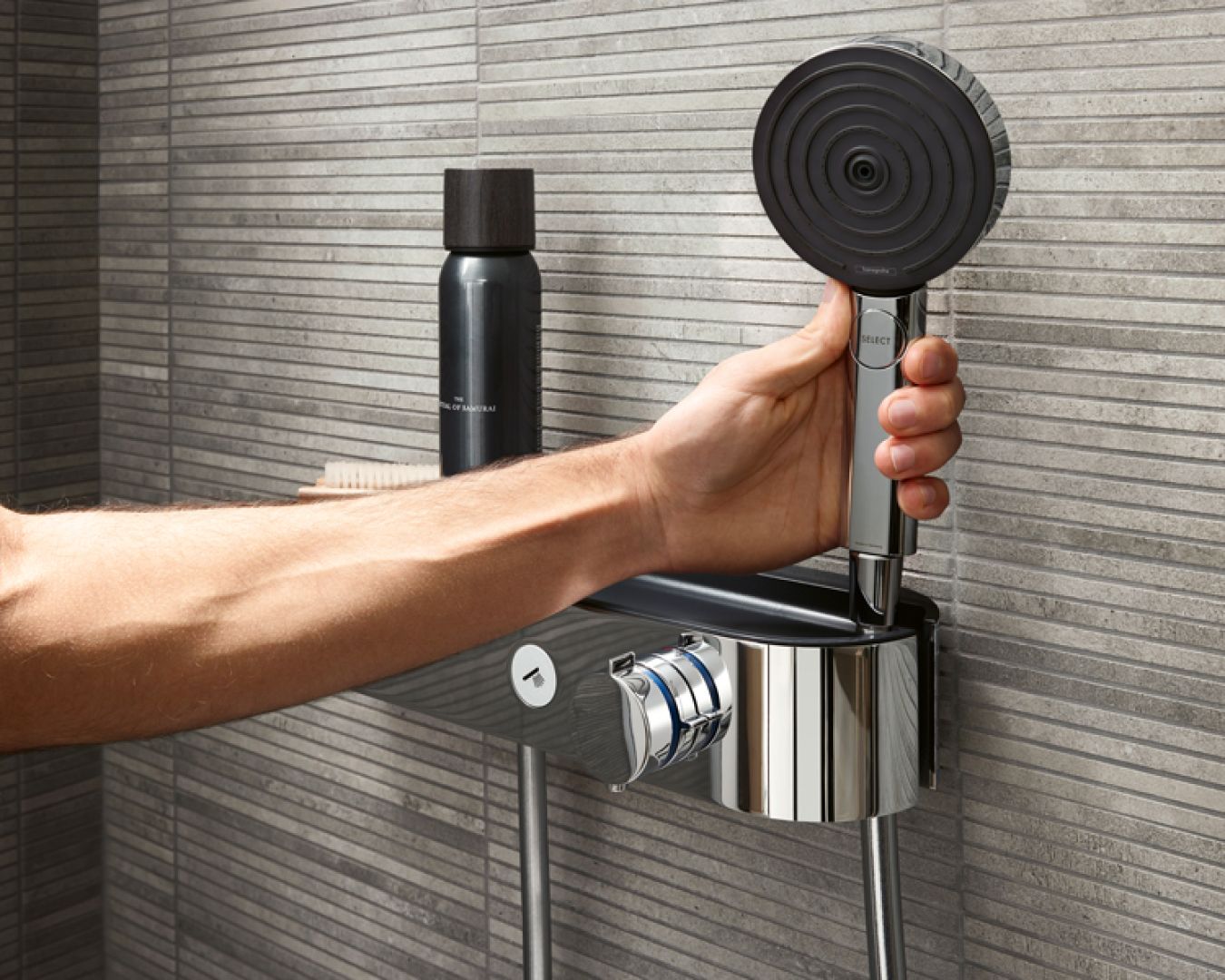 Hand nimmt moderne Handbrause von Duschablage mit grauen Wandfliesen