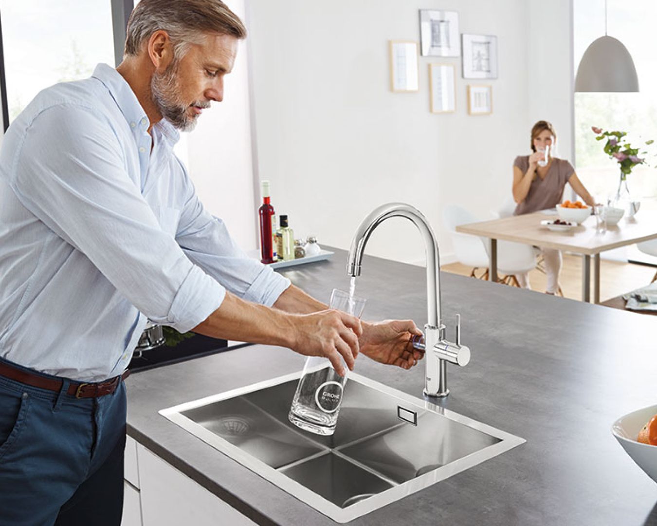 Mann füllt Trinkwasser aus moderner Küchenarmatur in eine Glaskaraffe