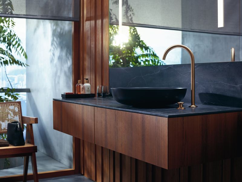 axor one Edles Bad mit dunklem Aufsatzbecken, Holzfront und goldener Armatur.