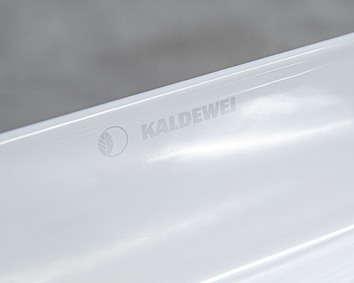 Prägelogo von Kaldewei auf weißer, glänzender  keramik Badoberfläche.