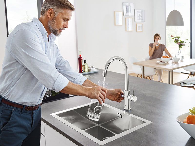 Mann füllt Trinkwasser aus moderner Küchenarmatur in eine Glaskaraffe