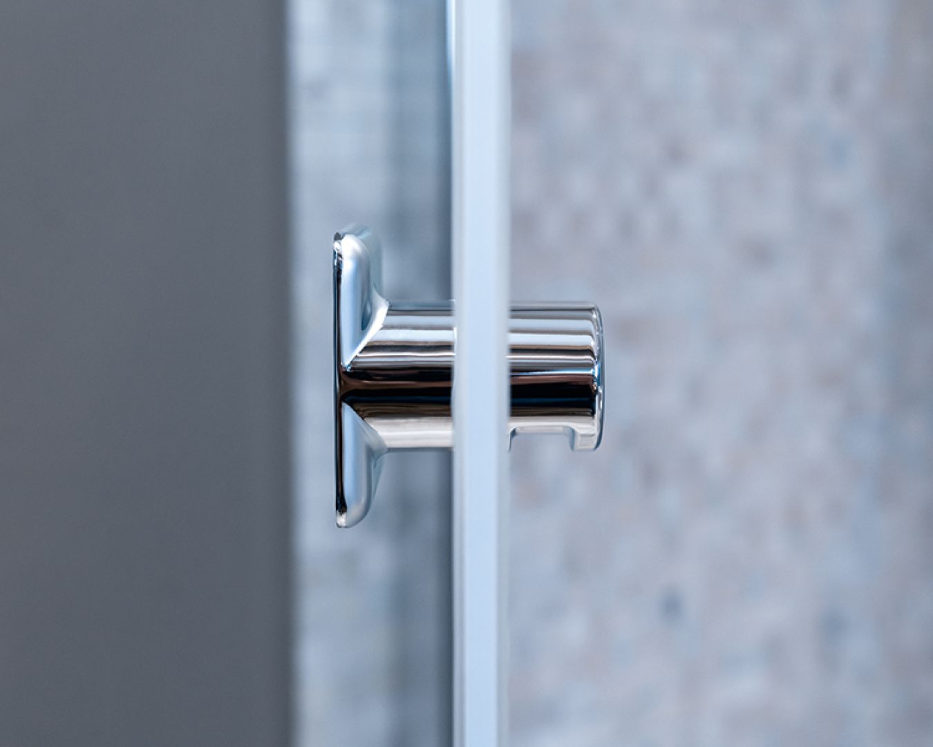 Verchromter Türgriff an einer Glasduschwand im Detail.