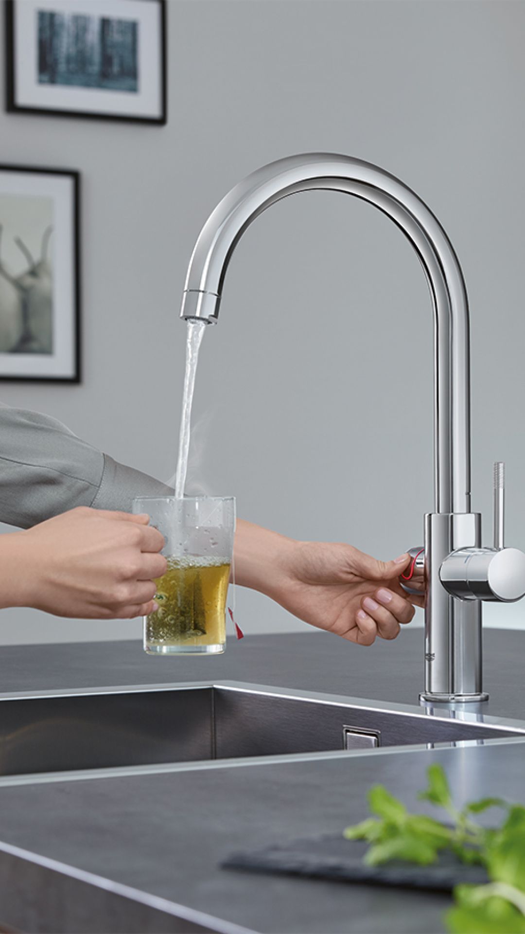 Frau zapft kochendes Wasser aus Armatur für ein Glas Tee in moderner Küche
