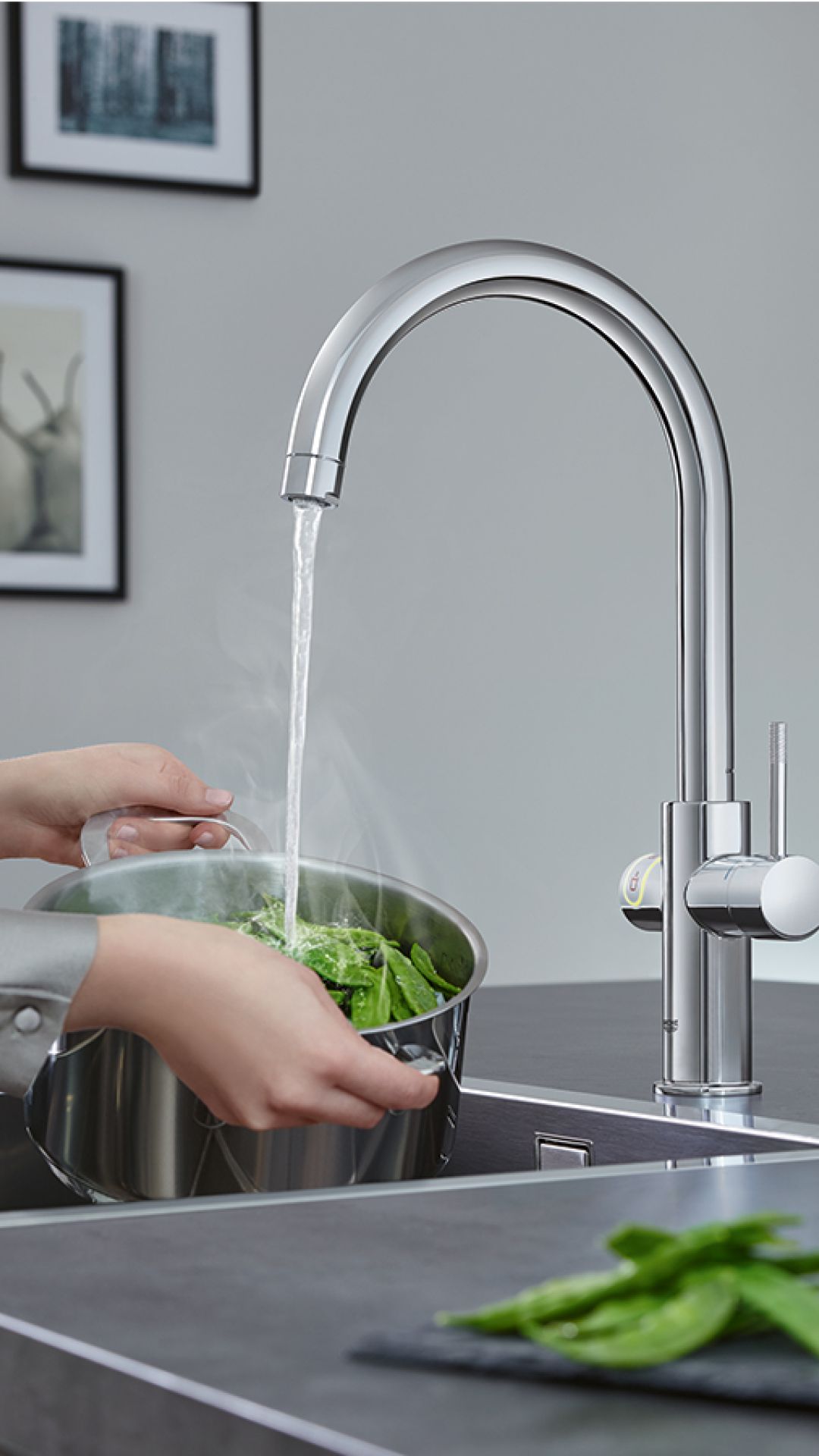 Heißes Wasser aus Küchenarmatur trifft auf frischen Spinat in Edelstahltopf