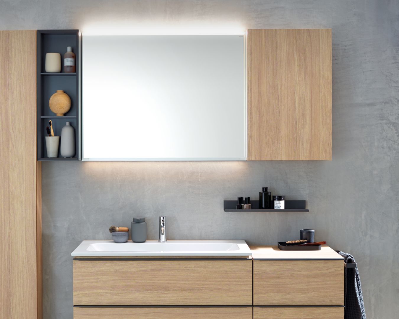 geberit Modernes Bad mit Holzfronten, beleuchtetem Spiegel und grauer Betonwand.