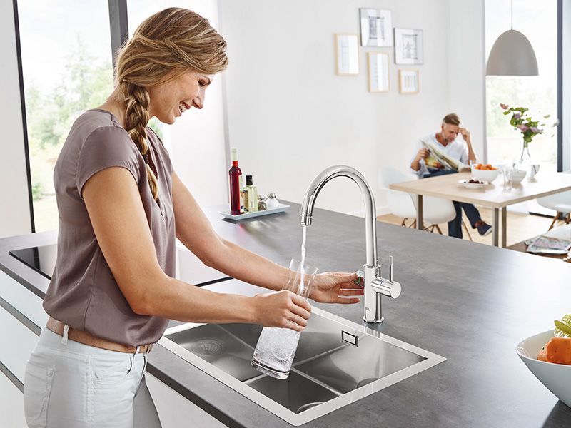 Frau füllt sprudelndes Wasser aus moderner GROHE Küchenarmatur in eine Glasflasche.