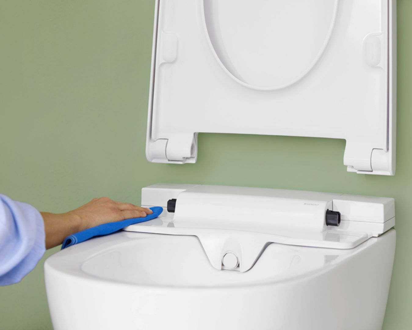 Person reinigt hygienisch die Oberseite eines Dusch-WCs mit Tuch.