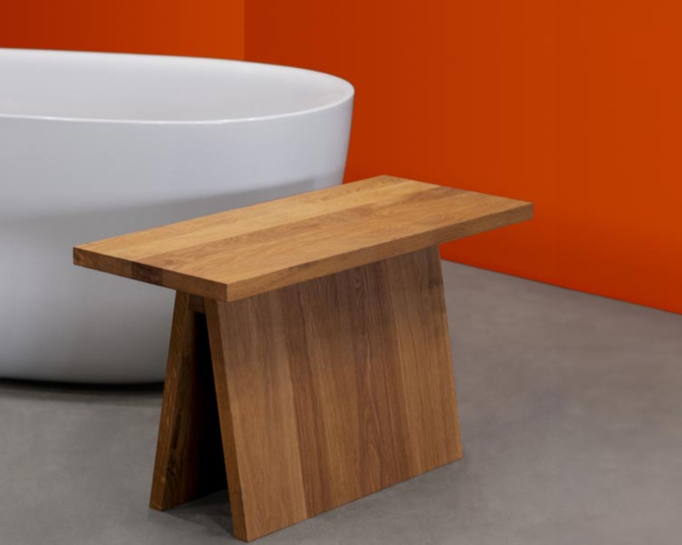 Minimalistische Holzbank vor freistehender Badewanne auf Betonboden

