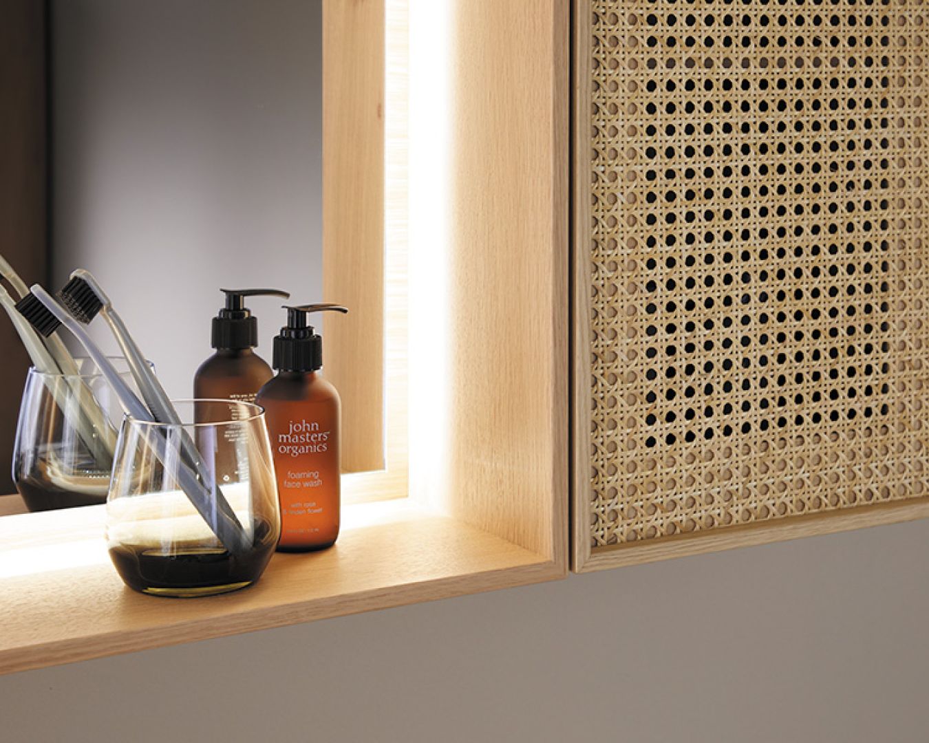 Detailaufnahme eines Badezimmers mit Zahnbürsten, Seifenspendern und Rattanschrank.