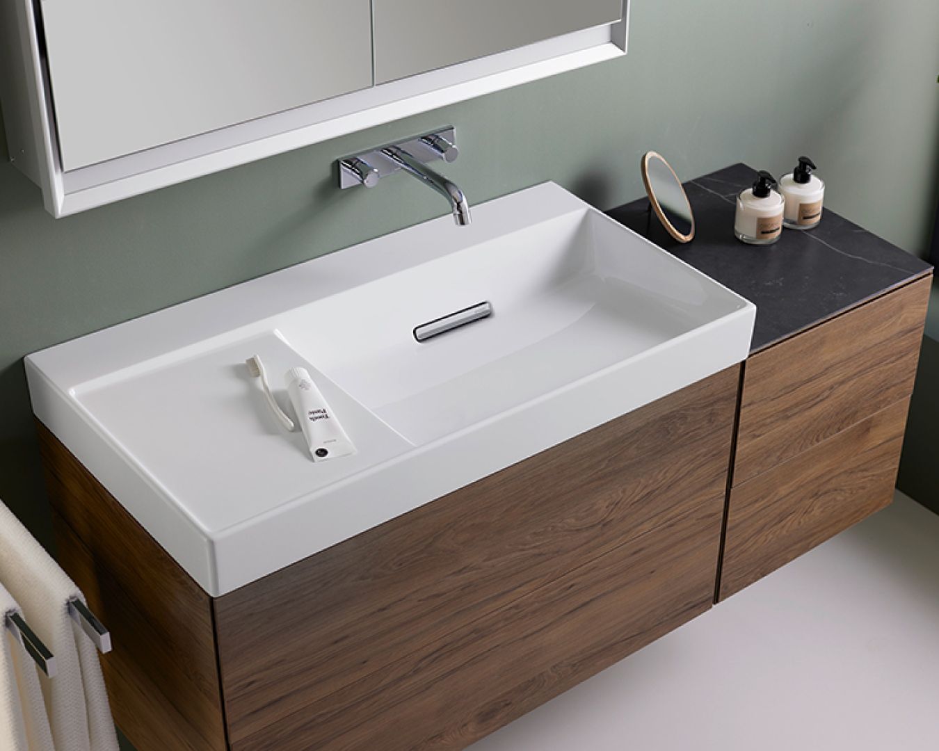 Modernes Waschbecken mit Holzunterschrank, Wandarmatur und Pflegeprodukten.