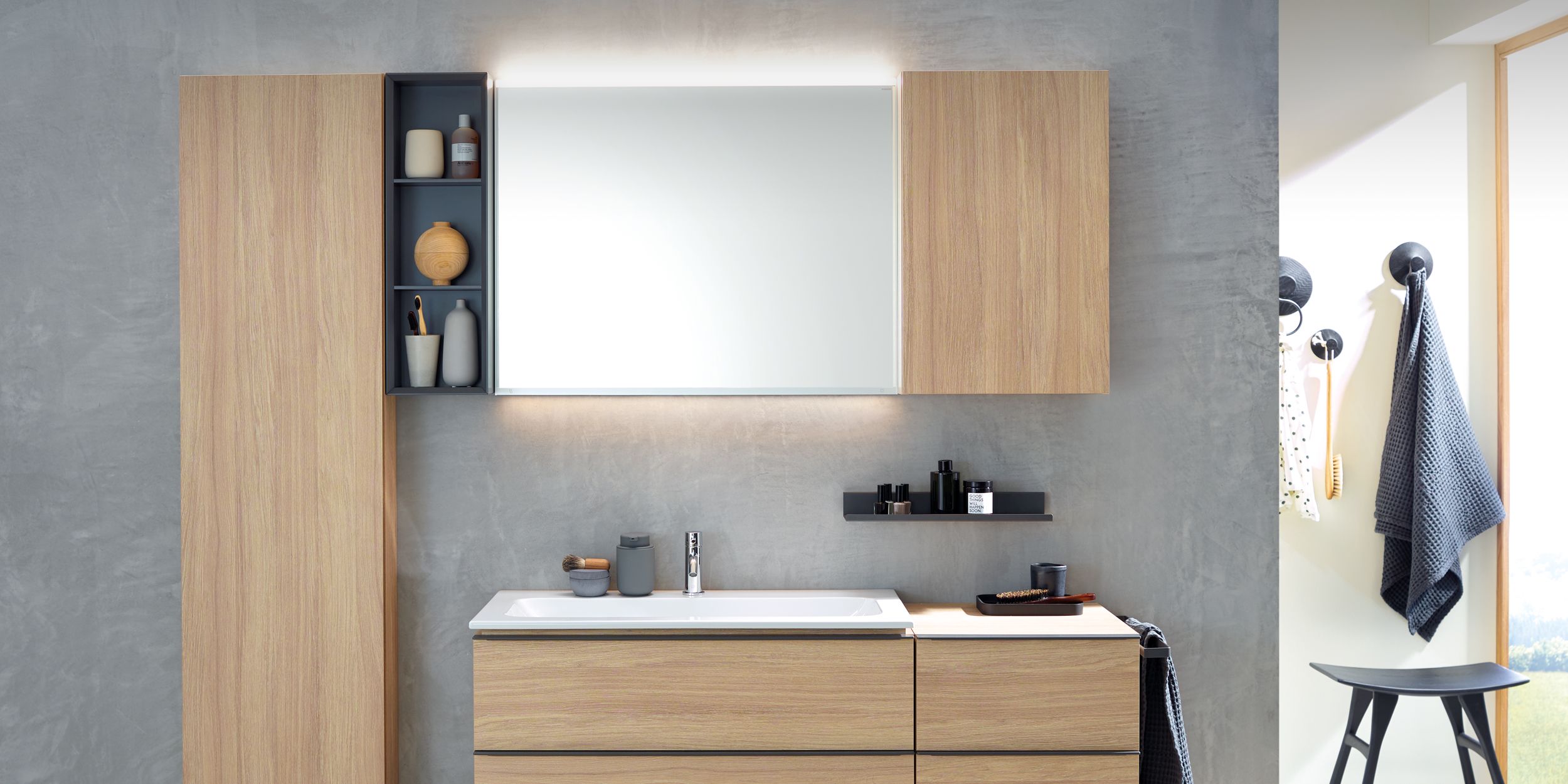 geberit Modernes Bad mit Holzfronten, beleuchtetem Spiegel und grauer Betonwand.