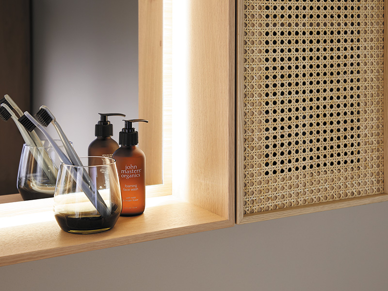 Detailaufnahme eines Badezimmers mit Zahnbürsten, Seifenspendern und Rattanschrank.