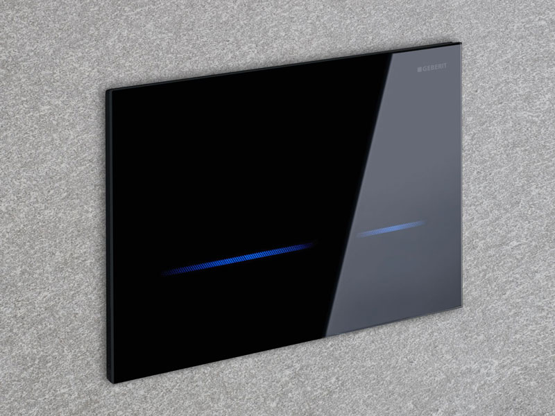 Schwarze WC-Spülplatte mit blauer LED-Leiste von Geberit an grauer Wand