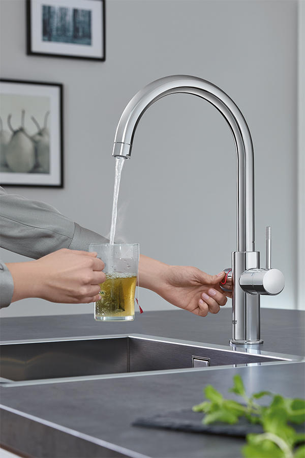 Frau zapft kochendes Wasser aus Armatur für ein Glas Tee in moderner Küche

