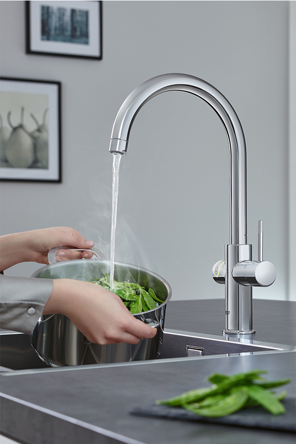 Heißes Wasser aus Küchenarmatur trifft auf frischen Spinat in Edelstahltopf
