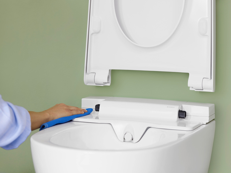 Person reinigt hygienisch die Oberseite eines Dusch-WCs mit Tuch.