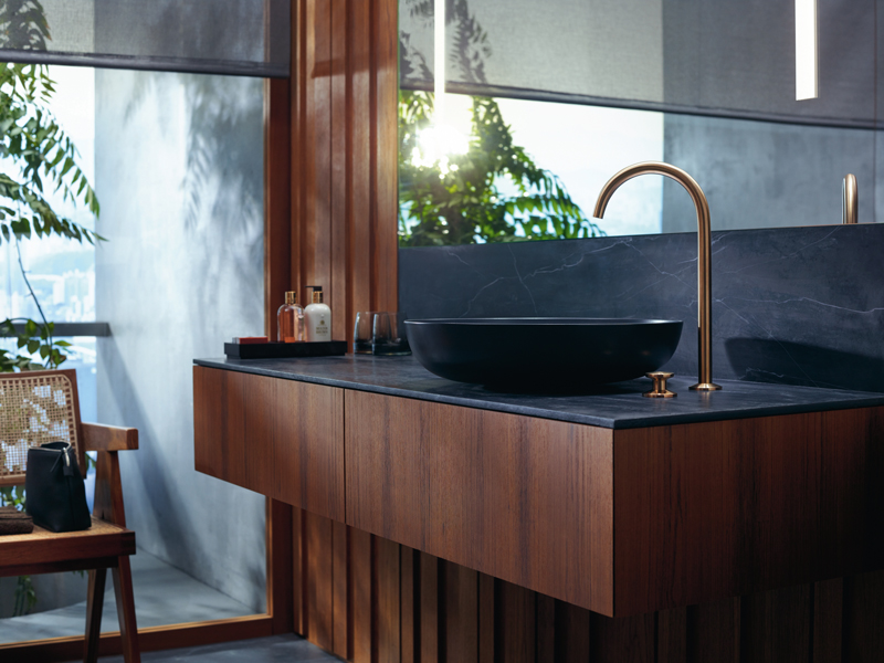 axor one Edles Bad mit dunklem Aufsatzbecken, Holzfront und goldener Armatur.