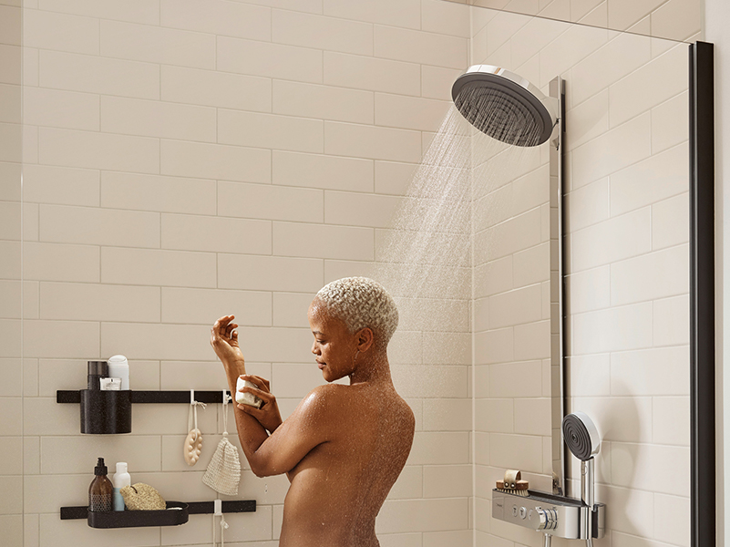 Hansgrohe Person mit kurzem Haar duscht unter moderner Regendusche in heller Fliesendusche.