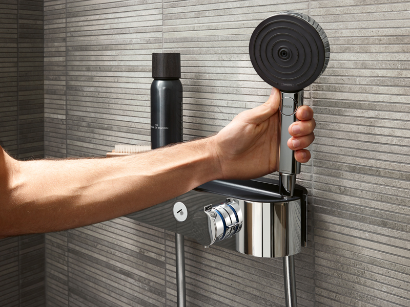 Hand nimmt moderne Handbrause von Duschablage mit grauen Wandfliesen
