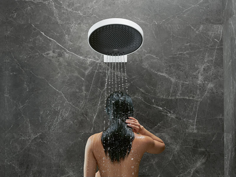 Frau unter Regendusche mit Wasserstrahl auf dunkler Natursteinwand